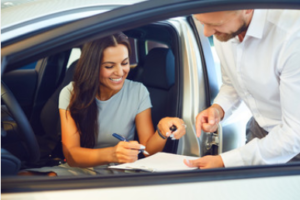 A woman is signing a car lease while sitting in her new car
